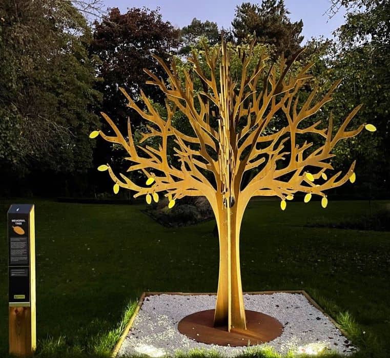 Verlichte gedenkboom heeft gouden gloed op het strooiveld van het crematorium